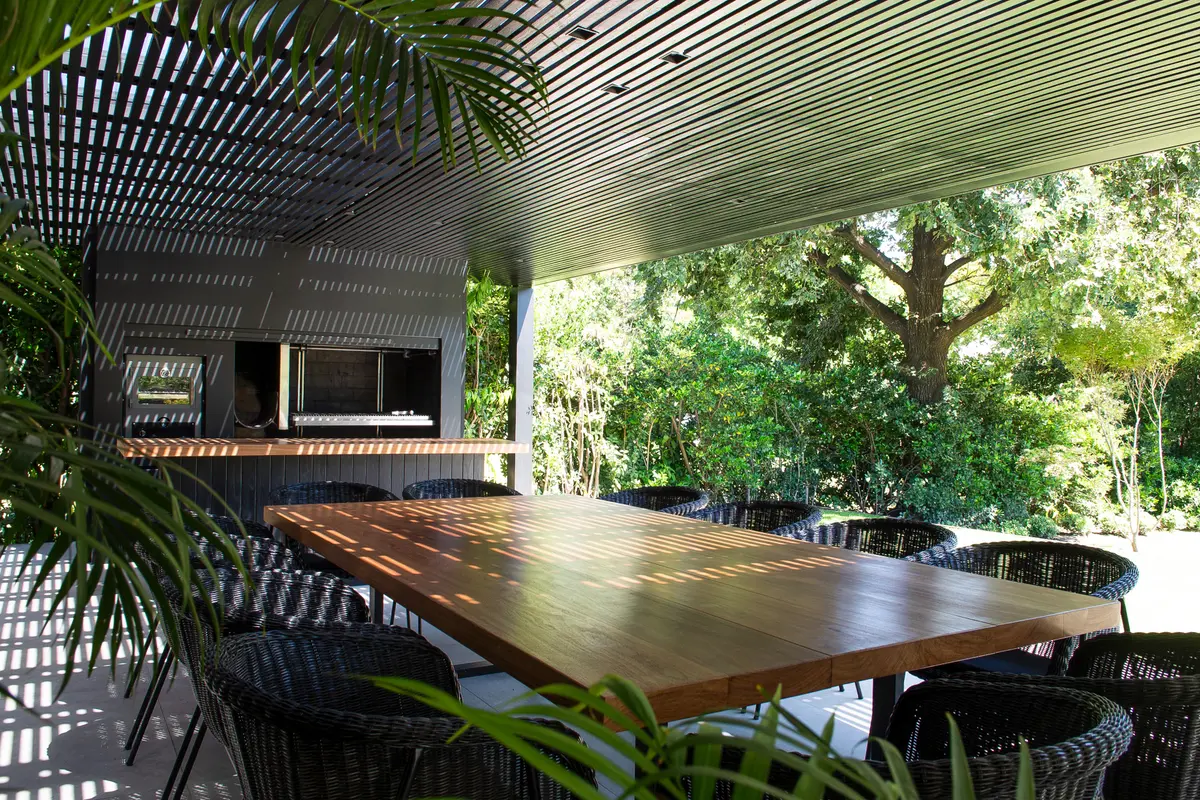 Sala de jantar externa moderna sob pérgola com vegetação exuberante — projeto Quincho SA, por Estudio Junor, em Pilar